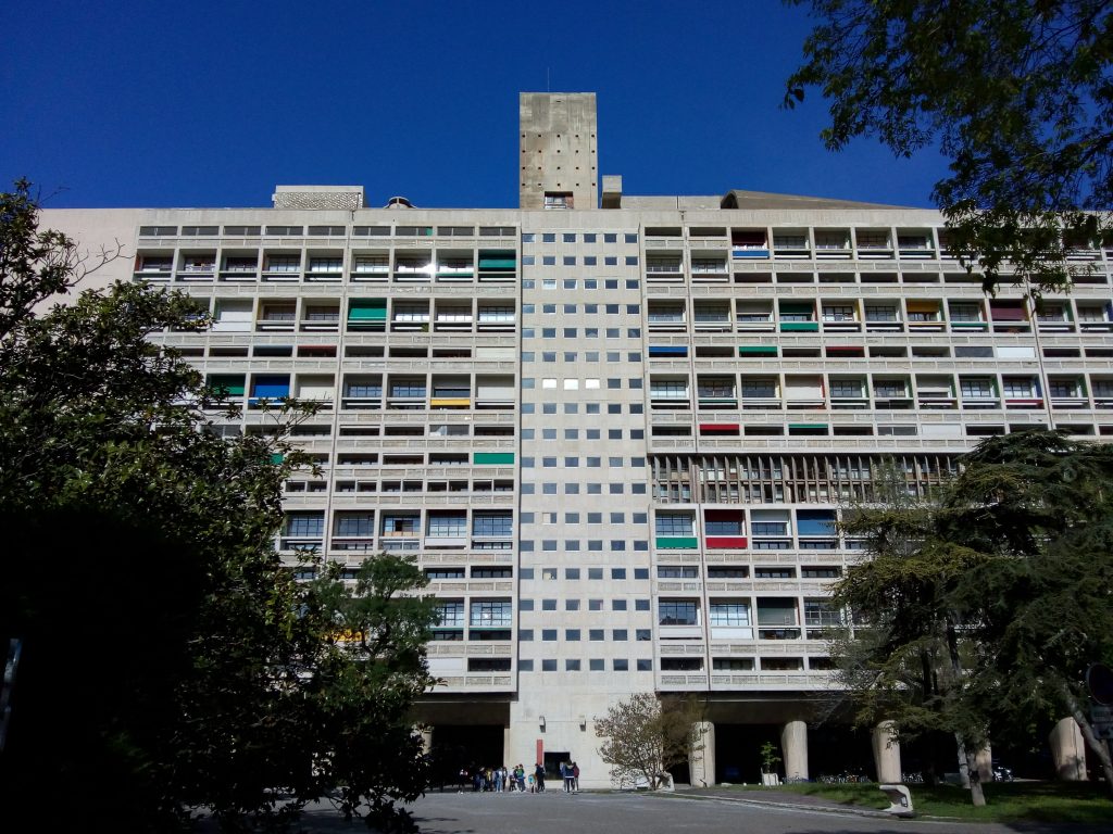 A arquitetura brutalista traz edifícios imponentes, porém, nem sempre despertam de imediato a paixão de todas as pessoas devido a suas formas mais pesadas e sem adornos. Suas características têm a ver com o momento social e econômico vivido por diversos países onde esse estilo arquitetônico floresceu. Conheça mais aqui. Brutalismo: arquitetura marcada pela hora da reconstrução O termo brutalismo surgiu do francês berton brut, que significa concreto bruto. Derivado da arquitetura moderna, a arquitetura brutalista esteve em alta entre os anos de 1950 e 1980, muito popular em projetos arquitetônicos institucionais, como escolas, órgãos públicos e também em projetos habitacionais. O estilo mais “bruto” sem acabamentos ou elementos decorativos nasceu justamente em um período de reconstrução das cidades dos países europeus após a Segunda Guerra Mundial. Portanto, na Europa Central e Oriental há muitos exemplos de edificações do estilo. Em total contraposição ao estilo ornamental criado na arquitetura antes da guerra, a ênfase era focar nos elementos funcionais das edificações ao invés de valorizar suas características estéticas. A aposta era em mais simplicidade e praticidade, com aplicação de materiais mais baratos e resistentes. Além disso, a necessidade também apontava para projetos que pudessem ser construídos rapidamente, com materiais fáceis de obter, por isso, o concreto entrou em cena. É interessante pensar que estava muito longe de existir a plataforma BIM, que permite construções mais rápidas e econômicas. Entre as características das obras da arquitetura brutalista, estão edificações com estilo geométrico, sem adornos, em blocos maciços na forma monolítica e com elementos modulares repetidos. Além disso, a paleta é predominantemente monocromática. É bastante comum que o brutalismo na arquitetura apresente estruturas suspensas, janelas que mais parecem buracos na parede e recortes bastante diferenciados e um tanto singulares. Nesse estilo de edificação, não há um compromisso em esconder os elementos da estrutura da obra, como vigas ou pilares. Mais tarde, a exposição desses elementos no estilo industrial ganhou certo charme. Porém, na arquitetura brutalista esses elementos não têm qualquer verniz estético. Com o tempo, esse estilo de arquitetura começou a ser considerado um estilo meio desajeitado, que muitos profissionais do setor fizeram questão de abandonar. Embora, seus defensores ainda costumem amar o estilo arquitetônico cru e áspero. Arquitetura brutalista brasileira internacional: obras marcantes Bem ao estilo ame ou odeie, há diversas edificações imponentes ao redor do mundo caracterizadas como brutalistas além da Europa, há exemplos também nos Estados Unidos, Canadá, Austrália, Japão e Israel. Apesar de o Brasil não ter sido um território de guerra, o estilo também influenciou a arquitetura do país, com diversos projetos concebidos com as características típicas em São Paulo e no Rio de Janeiro. Apesar da relevância da arquitetura brutalista para o contexto histórico, nos últimos anos, algumas obras brutalistas começaram a ser destruídas, como o edifício Robin Hood Gardens, em Londres, que tinha uma estrutura maciça de concreto, com 213 apartamentos. Vamos conhecer algumas delas no Brasil e no mundo: 1 - Unité d’Habitation (França) Renomado internacionalmente, o arquiteto e urbanista Le Corbusier foi quem consolidou o estilo a partir do projeto Unité d’Habitation, na França, iniciado em 1947 e concluído em 1952. Corbusier era um verdadeiro apaixonado pelas possibilidades do concreto e motivado pelas necessidades de moradia do pós-Guerra, Corbusier concebeu esse edifício como uma cidade-jardim vertical com capacidade para unidades independentes para 1.600 residentes . 2 - Trellick Tower (Inglaterra) Situada em Londres, a torre foi concluída em 1972, com um grande bloco com 31 andares. A estrutura de concreto foi concebida com 100 metros de altura, com elevadores e escadas separadas dos apartamentos. Passou por várias reformas, mas foi classificado como Grade II pelo patrimônio inglês. Sofreu um grande incêndio em 2017, mas ainda é um dos grandes exemplos de arquitetura brutalista no cenário londrino. 3 - The Barbican (Inglaterra) Também situado em Londres, o complexo habitacional moderno The Barbican foi projetado após um ataque aéreo no coração do distrito financeiro da capital. Onde só havia escombros, surgiram 2.000 apartamentos para abrigar trabalhadores, escolas, cinema e restaurante. Além do concreto como protagonista, muitos apartamentos ainda têm cozinhas originais com superfícies em aço inoxidável e banheiros com pias de mão. 4 - Western City Gate (Sérvia) Essa edificação em Belgrado é composta por duas torres de concreto ligadas no topo por uma ponte de dois andares. A aspereza do concreto monumental neste arranha-céu dá uma aparência de edificações vistas em produções de ficção científica. Na verdade, essa é uma característica que faz parte de Belgrado como um todo. 5 - Habitat 67 (Canadá) Situado em Montreal, o Habitat 67 também foi uma solução habitacional conceitual para resolver a questão das moradias. O edifício foi concebido com mais de 350 módulos iguais em concreto, que foram dispostos de uma forma diferente, que resultou em uma formação de 12 andares, edificados de uma forma suspensa que dá a impressão de uma brincadeira de montar do jogo de Lego. Wikimedia Commons 6 - Edificio J. Edgar Hoover (FBI - Chicago) Entre alguns exemplos de obras poderosas marcadas pelo estilo brutalista estão o edifício J. Edgar Hoover, conhecido por ser o quartel-general do FBI, em Chicago (EUA), projetado na década de 1960. No entanto, com o tempo, esse prédio maciço e monumental passou a ser pouco apreciado pelos milhares de funcionários e a mudança do FBI de casa começou a tomar conta dos noticiários. 7 - Prefeitura de Boston (EUA) Diante do declínio econômico do pós-Guerra, o edifício monumental da Prefeitura de Boston também foi concebido na década de 1960. O prédio, projetado por Gerhard Kallmann e Michael McKinnell, recebeu grande influência do estilo de Le Corbusier, apresenta módulos angulares e salientes, e tem fachada em estilo de grade. 8 - Tribunal de Contas do Município de São Paulo (SP) A arquitetura brutalista paulista tem exemplos de edificações expressivas como o Tribunal de Contas do Município de São Paulo. Reserva todas as características próprio da arquitetura, inclusive os recortes singulares. O edifício quadrado, edificado com concreto armado aparente, tem 3 pavimentos e é sustentado por colunas ocas. 9 - Sesc Pompeia (São Paulo) O Sesc Pompeia (São Paulo -SP) é um exemplo de arquitetura brutalista no Brasil. Foi a arquiteta Lina Bo Bardi a encarregada de transformar uma fábrica de tambores em um complexo cultural. O prédio apresenta grandes estruturas em concreto, com paredes sem acabamento, com materiais simples, apenas jateadas com areia. Além disso, suas torres de concreto rígido são ligadas por passarelas aéreas e entrecruzadas. Na concha externa, a antiga estrutura de madeira da ex-fábrica ainda pode ser visualizada. 10 - Prédio da FAU/USP O prédio da Faculdade de Arquitetura e Urbanismo da Universidade de São Paulo (FAU/USP) também foi concebido no estilo brutalista. O prédio traz concreto bruto, vidro e linhas simples, com ênfase em integração de espaços e funcionalidade. O prédio é sustentado por pilares, que são levemente apoiados no chão, e têm forma de trapézios. Não há portas de entrada para marcar a grande liberdade de movimentação da instituição universitária. 11 - MASP (SP) O Museu de Arte de São Paulo (MASP) traz a edificação monumental em concreto, o minimalismo nos detalhes, os recortes singulares, o vão livre e a estrutura suspensa como um dos prédios mais marcantes da arquitetura brutalista paulista. 12 - MAM (RJ) Apesar do estabelecimento da arquitetura brutalista em São Paulo, o Museu de Arte Moderna do Rio de Janeiro foi onde esse estilo teve seu início no Brasil. O MAM foi a primeira obra de concreto aparente do país. Lá estão presentes, o concreto, as grandes janelas com vidro e as colunas monumentais. O projeto é de Affonso Eduardo Reidy.